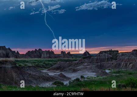 An active lightning storm over the mountains of Badlands National Park in South Dakota lights up the sky against a colorful horizon. Stock Photo