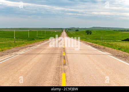 Diminishing perspective of a rural road in the Great Plains surrounded by green farmland and vast lands. Stock Photo