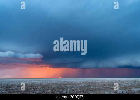 A large storm moves across the Great Plains as the sun sets behind it while rain and lightning line the horizon. Stock Photo