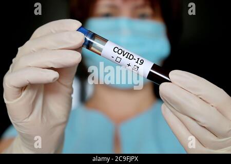 Test tube with covid-19 blood sample in female hands close up, woman in medical mask and gloves holding a vial. Doctor with positive test Stock Photo