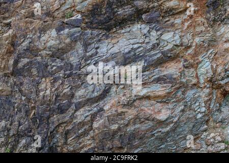 The rock texture is gray, blue, brown and black. There are small inclusions of plants. Stock Photo