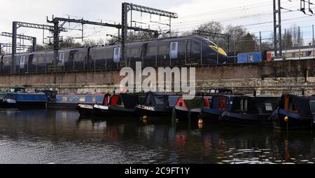 A Javelin train passes canal boats moored in Regent's Canal as it leaves Saint Pancras station in London Stock Photo