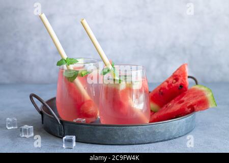 Summer cold drink with watermelon, mint leaves and ice on a vintage tray. Two glasses with eco bamboo straws Stock Photo