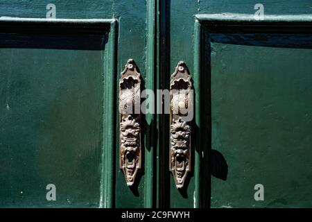 Patterned metal door handles on green double-leaf doors. Stock Photo