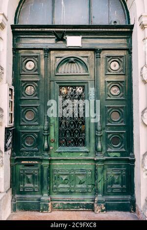 Carved green wooden doors with glass, pillared and narrow, outside in the facade of a building on a street in Budapest in Hungary. Stock Photo
