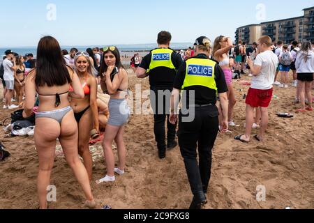 Edinburgh, Scotland, UK. 31 July, 2020. Temperature of 25C and sunshine brought huge crowds to Portobello Beach outside Edinburgh. Several large groups of teenagers were enjoying beach and alcoholic drinks were very popular. Pictured; At approx 3pm trouble broke out between young people on the the beach and police. Police reinforcements were quickly on scene and several people were apprehended. Westbank Street was closed to traffic and approx 30 police are patrolling the promenade. Police are confiscating alcohol from the teenagers remaining got the beach.  Iain Masterton/Alamy Live News Stock Photo