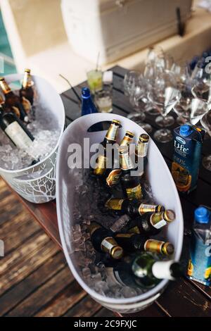 Two ice buckets full of beer bottles for a party on a wooden table with empty martini glasses and cans of juice. Stock Photo