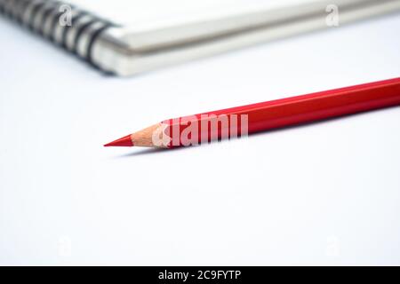 Red color wood pencil crayon placed in front of a white colored note paper diary Stock Photo