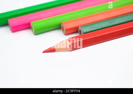 Six different colored wood pencil crayons placed on top of a white paper background Stock Photo