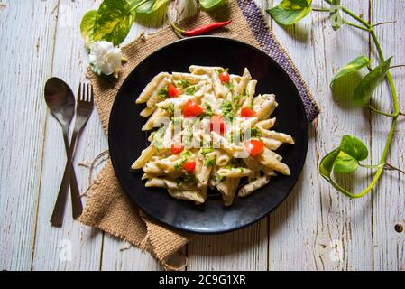 cooked penne pasta served on a black plate with condiments with use of selective focus Stock Photo