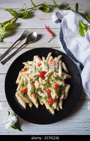 Top view of cooked penne pasta served on a black plate with condiments Stock Photo