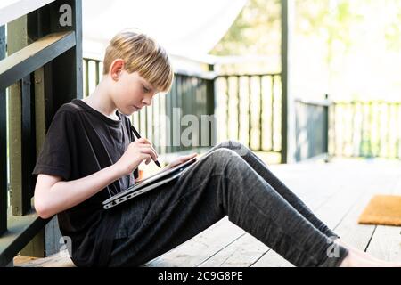 Young person sitting on porch outside using tablet and stylus Stock Photo