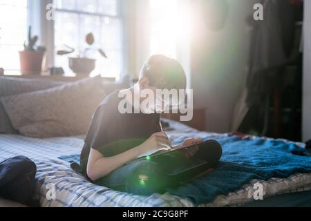 Tween sitting on bed working on laptop with touchscreen and stylus Stock Photo