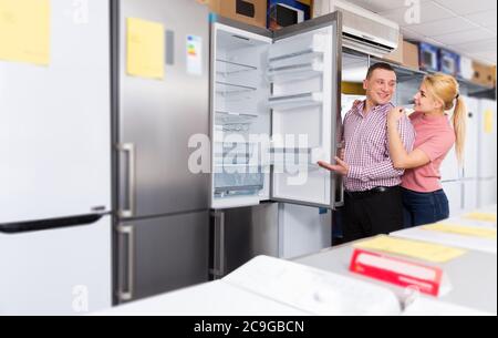 Positive couple chooses refrigerator in shop of household appliances Stock Photo