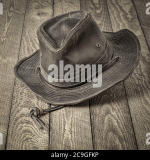 weathered outback oilskin hat hanging on rustic wooden table monochromatic image in square format Stock Photo