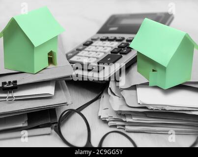 Two small green paper houses on a pile of document and files and a calculator. Stock Photo