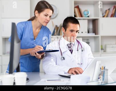 Two focused physicians working with case histories on laptop in modern office Stock Photo