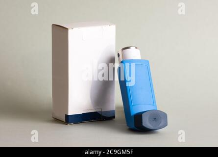 Closeup shot of an asthma blue inhaler leaned on its box on the gray background Stock Photo