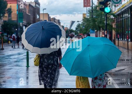 Montreal, CA - 30 July 2020: People on Mont-Royal Avenue holding umbrellas during rain & storm Stock Photo