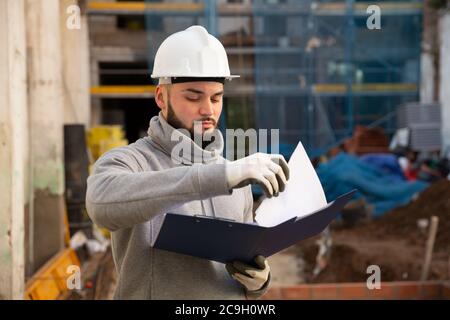Young bearded foreman making task list during works in building under construction Stock Photo