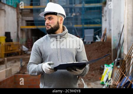 Young bearded foreman making task list during works in building under construction Stock Photo