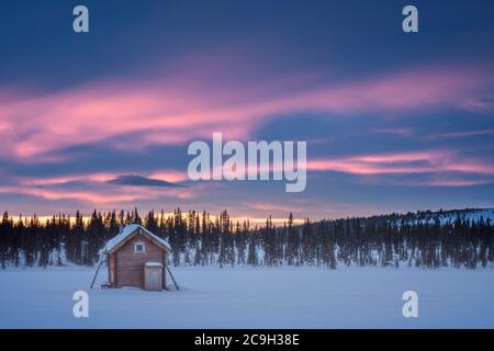 Small wooden hut on a wide snow-covered plain at extremely low temperatures at dawn, Skaulo, Norrbottens laen, Sweden Stock Photo