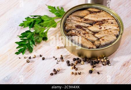 Appetizing smoked sprats in oil in open tin can on wooden table. Traditional canned fish Stock Photo
