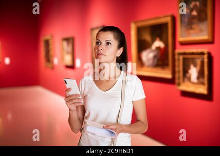 Portrait of young female visitor using phone in paints exposition at museum Stock Photo