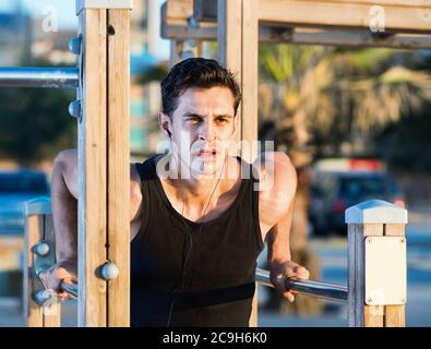 Happy cheerful positive  strong man doing parallel bar dips to music on sports ground on beach Stock Photo