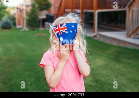 Adorable cute happy Caucasian girl holding Australian flag. Funny child kid covering her face with Australia flag. Little citizen celebrating Australi Stock Photo