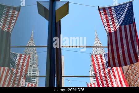 New York, June 30, 2018: Chrysler Building crown reflected in window seen through American Flags, focus on the crown. Stock Photo