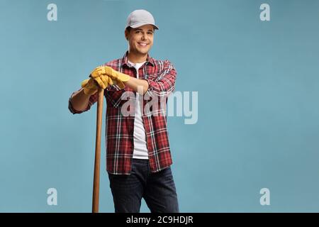 Young male farmer leaning on a wooden stick isolated on a blue background Stock Photo