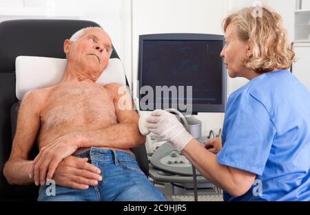 Smiling pleasant female technician diagnosing male patient using modern ultrasound scanner in private clinic Stock Photo