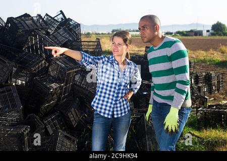 Man and women farm workers discussing working process pointing to something near empty boxes Stock Photo