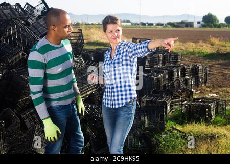 Man and women farm workers discussing working process pointing to something near empty boxes Stock Photo