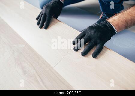The master mounts the laminate on the floor - a long row assembled from panels along the entire length joins the previous one Stock Photo