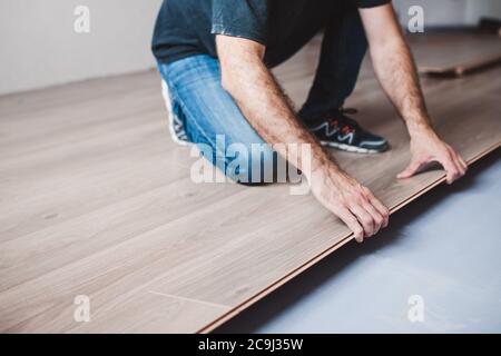 The master mounts the laminate on the floor - a long row assembled from panels along the entire length joins the previous one Stock Photo