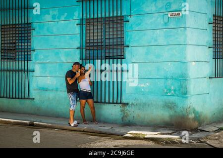 Havana, Cuba, July 2019, a young couple by a turquoise wall in Calle Aguiar taking a selfie in the oldest part of the city Stock Photo