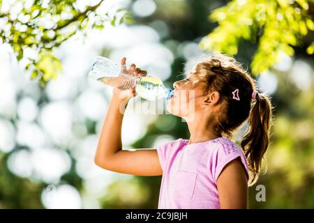 Girl drinking water from plastic bottle in park. Stock Photo