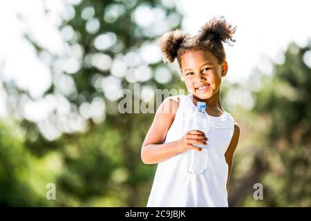 Girl standing with water bottle in park, smiling, portrait. Stock Photo