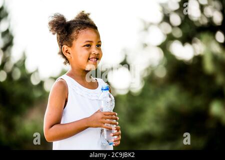 Girl standing with water bottle in park, smiling, portrait. Stock Photo