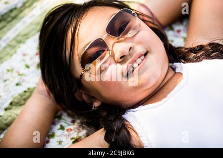 Girl lying on blanket in park, smiling, portrait. Stock Photo