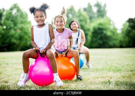 Girls bouncing on inflatable hopper in park, smiling. Stock Photo