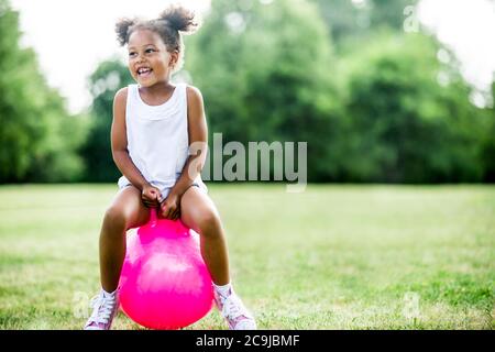 Girl bouncing on inflatable hopper in park, laughing. Stock Photo