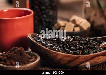 Red coffee cup, coffee beans and ground coffee in wooden bowl on table. Making coffee concept. Stock Photo