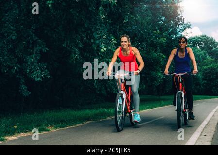 Two women riding bicycles together in park. Stock Photo