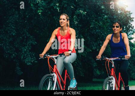 Two women riding bicycles together in park. Stock Photo