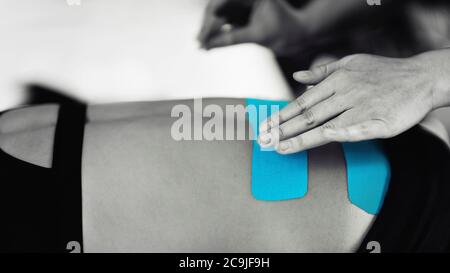 Physical therapist placing kinesio tape on patient's back. Stock Photo