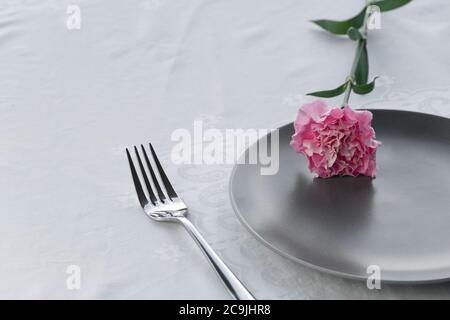 dark grey plate with natural pink carnation flower for food restaurant service background Stock Photo