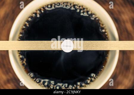 Cup of black coffee and caffeine pill on wooden spoon. Stock Photo
